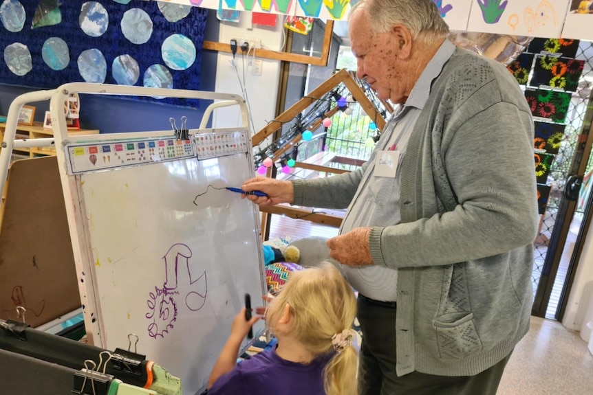 Older gentleman draws at a whiteboard with a child