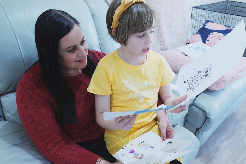 A young girl sits on her mothers knee, showing her drawings of animals