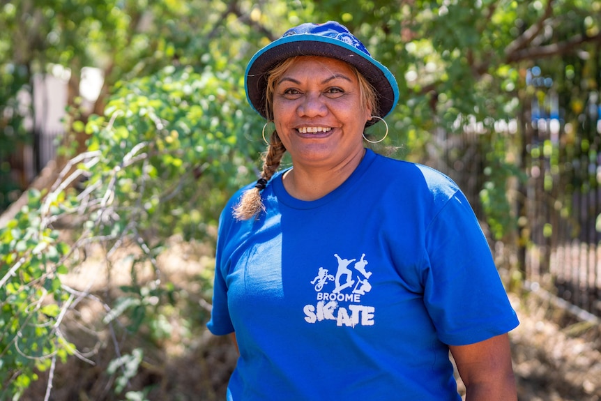 A woman in a blue shirt and hat smiles at the camera