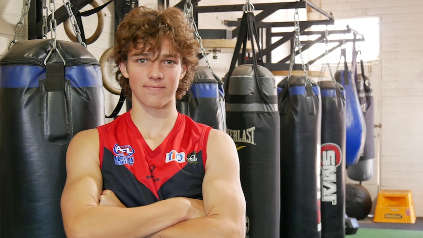 A male teenager stands with crossed arms in a boxing gym