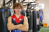 A male teenager stands with crossed arms in a boxing gym