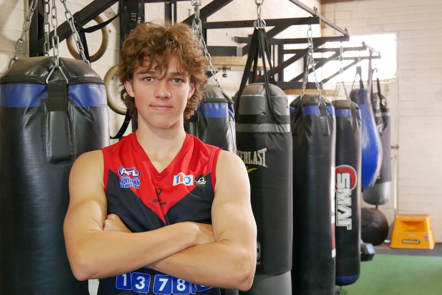 A male teenager stands with crossed arms in a boxing gym