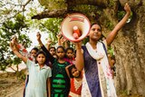 A group of girls in India standing together with their fists held in the air, and one holding a megaphone.
