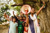 A group of girls in India standing together with their fists held in the air, and one holding a megaphone.