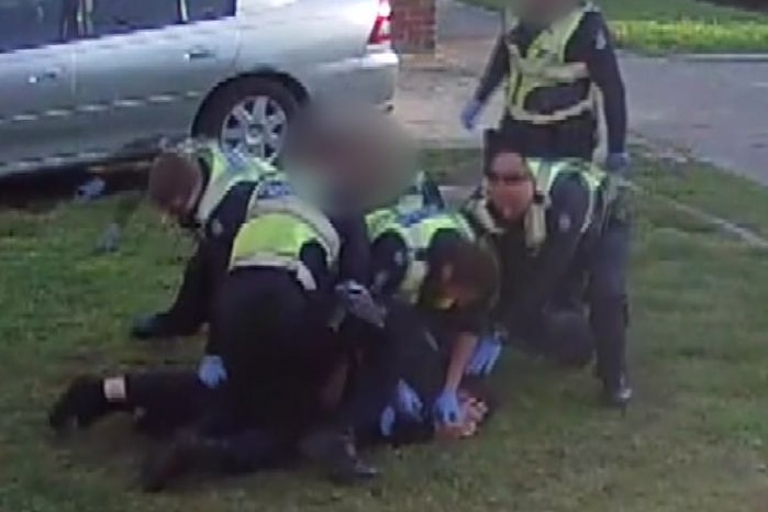 Police officers are shown on top of a man on the lawn outside his home.