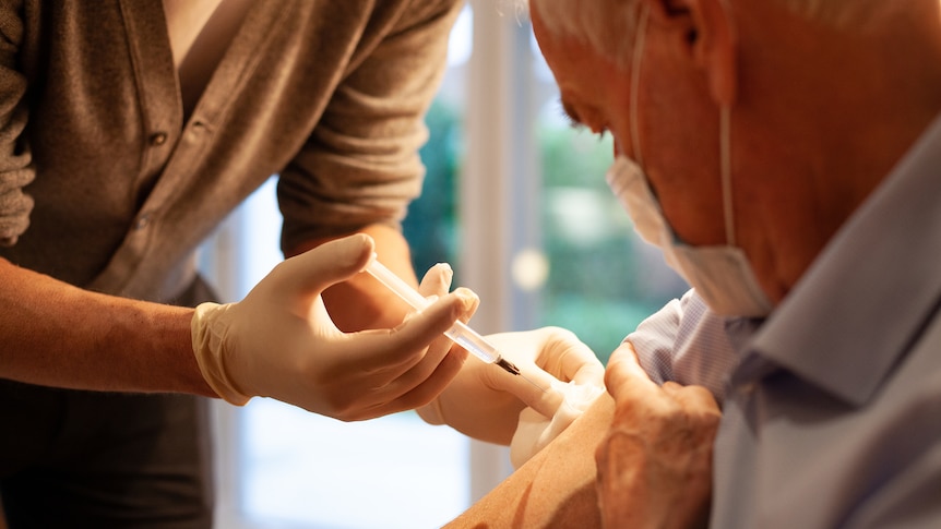 Senior man wearing a shirt receives an injection in his arm.