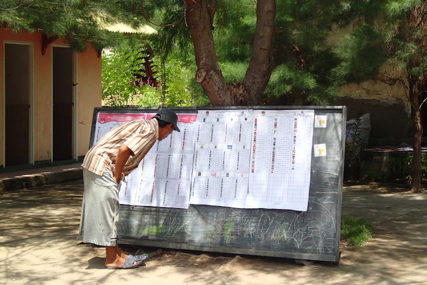 A man standing and observing a board with list of candidates during a local election in 2014.