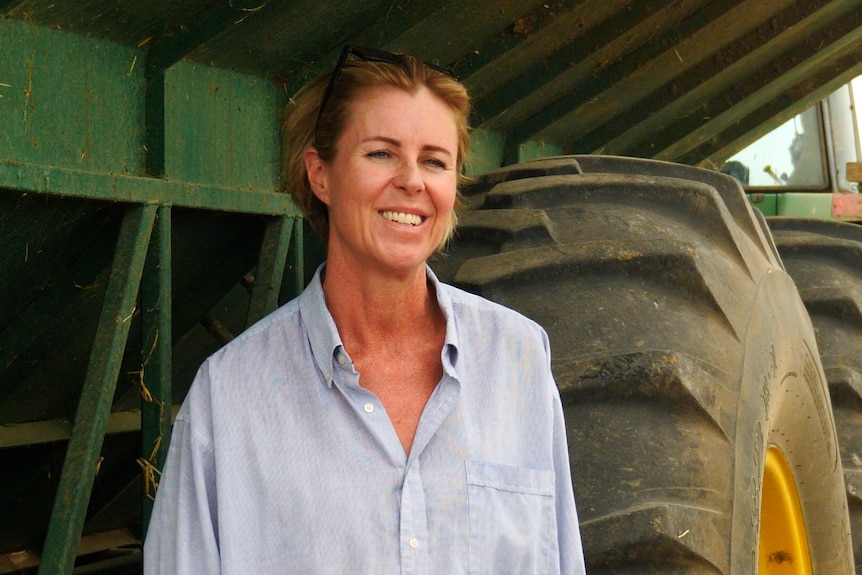 Woman in button-up shirt stands in front of a tractor.