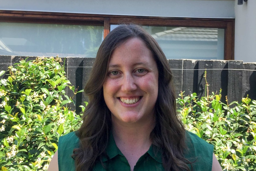 A smiling woman in a green top in front of a fence and hedge