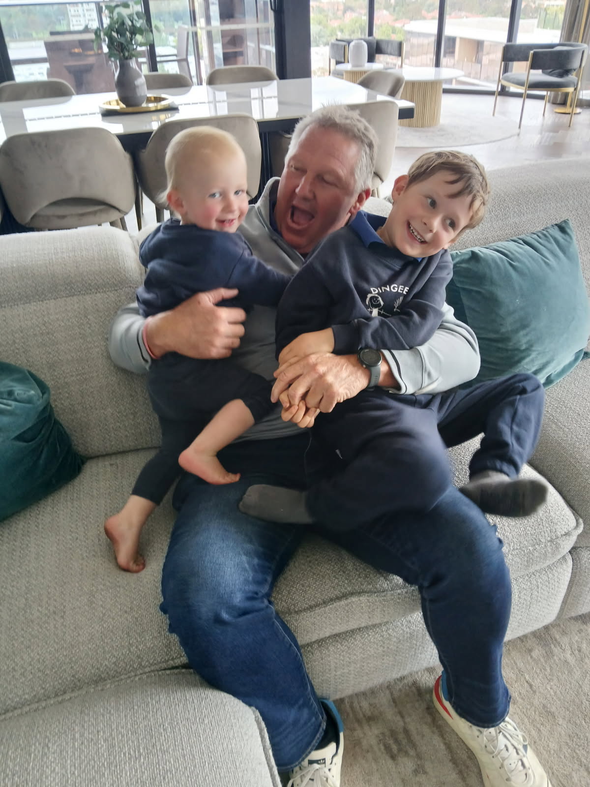 A man with an open mouthed expression sitting on a family couch, holding two smiling children