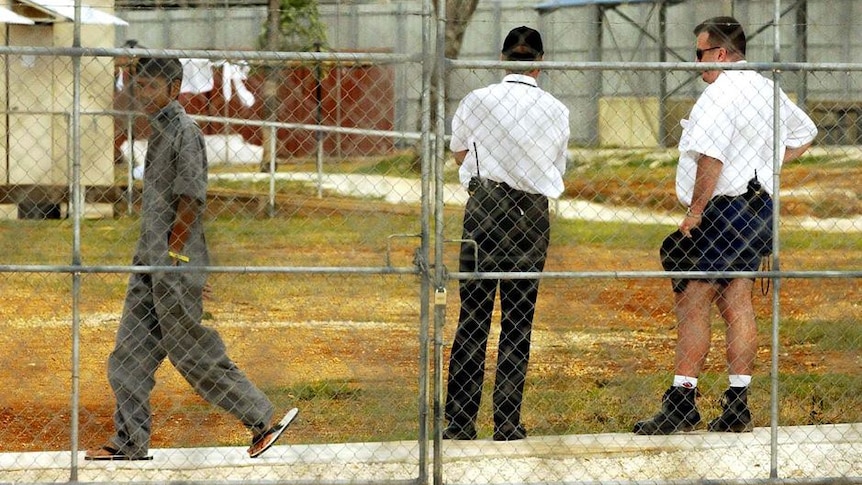 Two guards look on as an asylum seeker walks by at the Christmas Island Detention Centre.