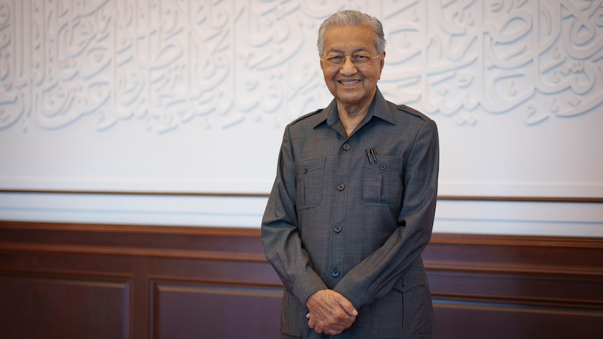 Mahathir Mohamad standing in front of a white and brown wall