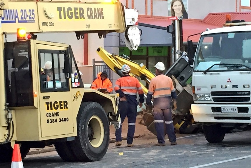 Workers and a crane at the scene of a road hole