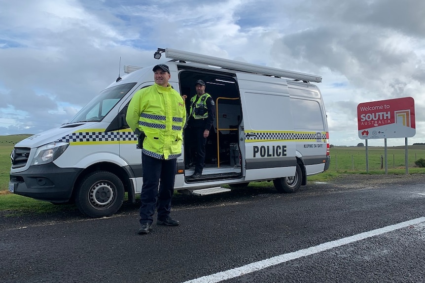 A policeman stands near a van and one inside a van next to a sign about entering South Australia