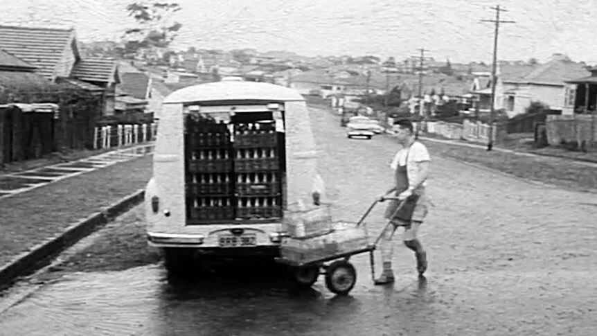 Old photo of milk delivery man with wheelbarrow at the back of delivery van in the street