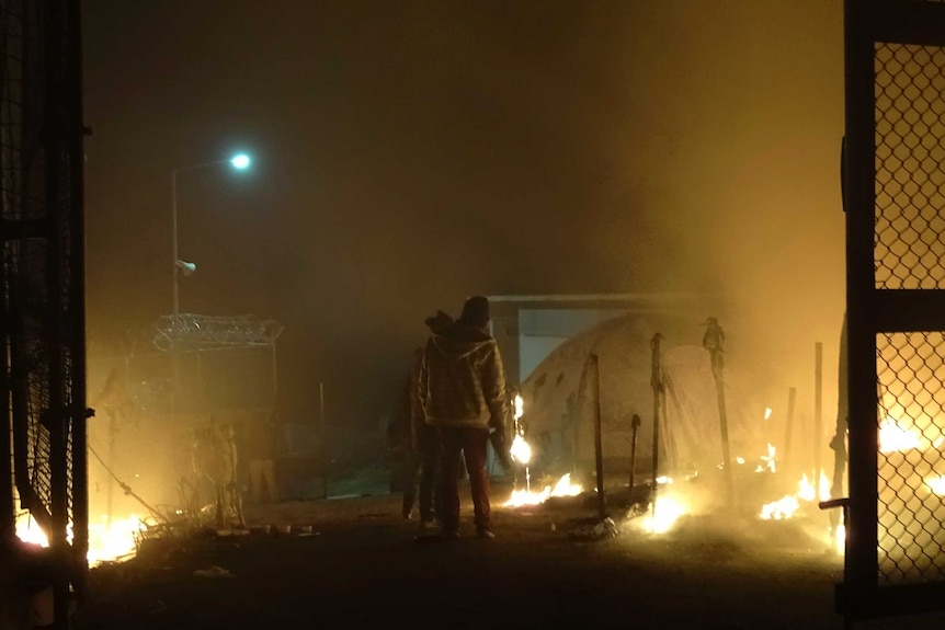 Refugees stand next to burning tents at the Moria refugee camp.