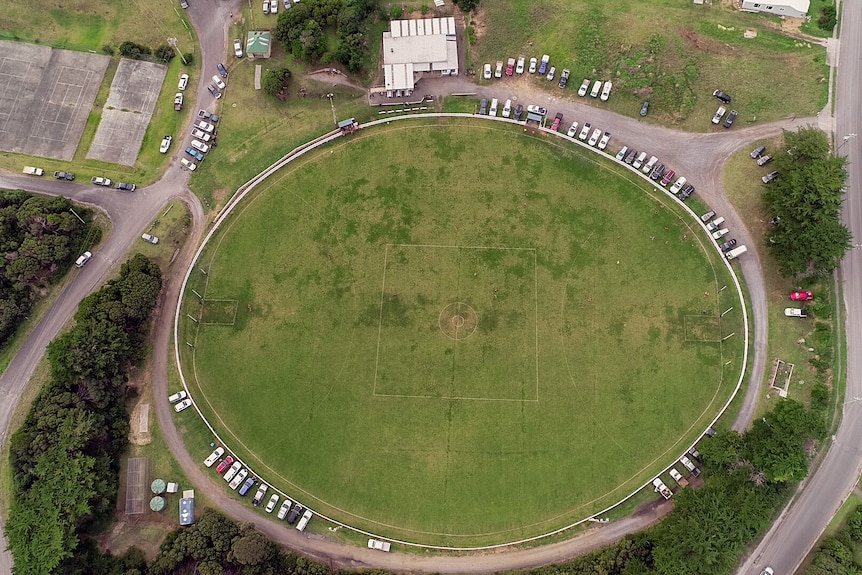 An aerial drone shot of a small country football ground with cars parked around the perimeter 