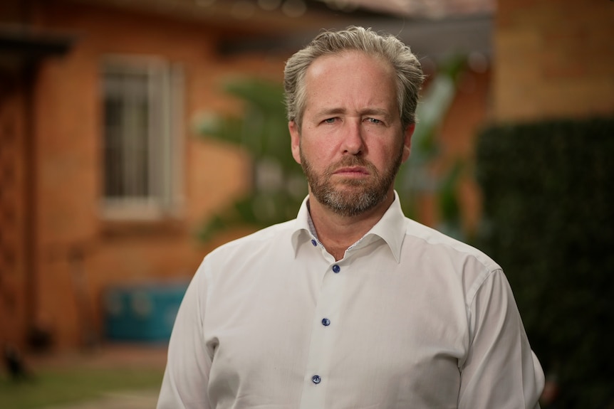 An image of Ben Cannon in a white shirt in front of a blurred brick building