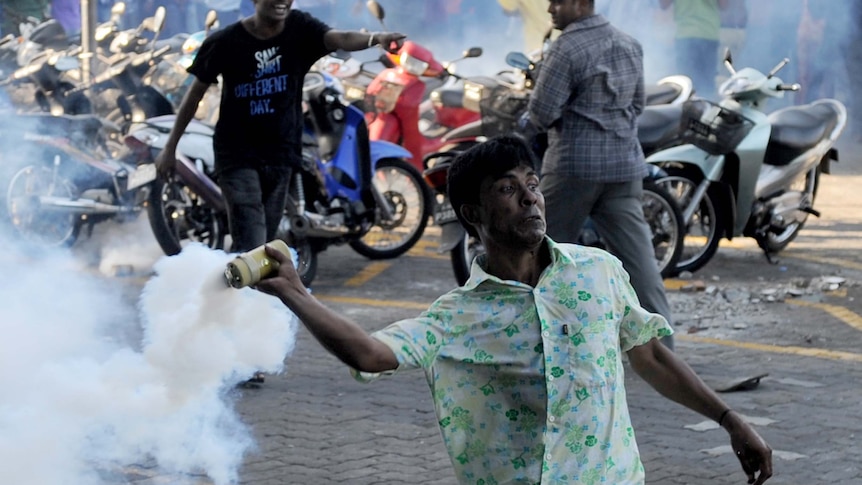 An anti-government protester throws a tear gas canister at police during clashes in the Maldives
