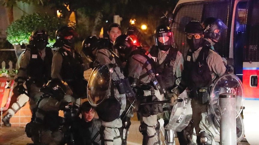 Heavily-protected Hong Kong police surround a bleeding protester in the street