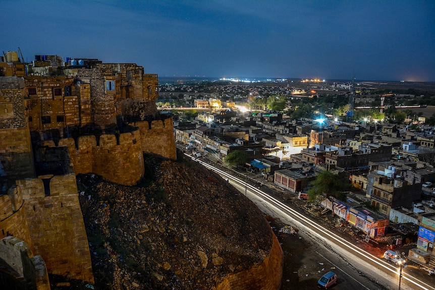 Old stone buildings overlook a city of twinkling lights at night.