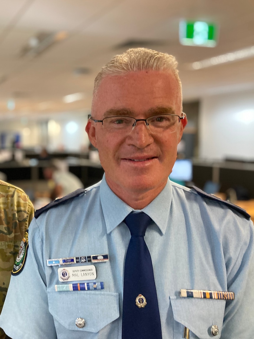 Man in khaki uniform standing next to man in blue police uniform,wearing glasses.