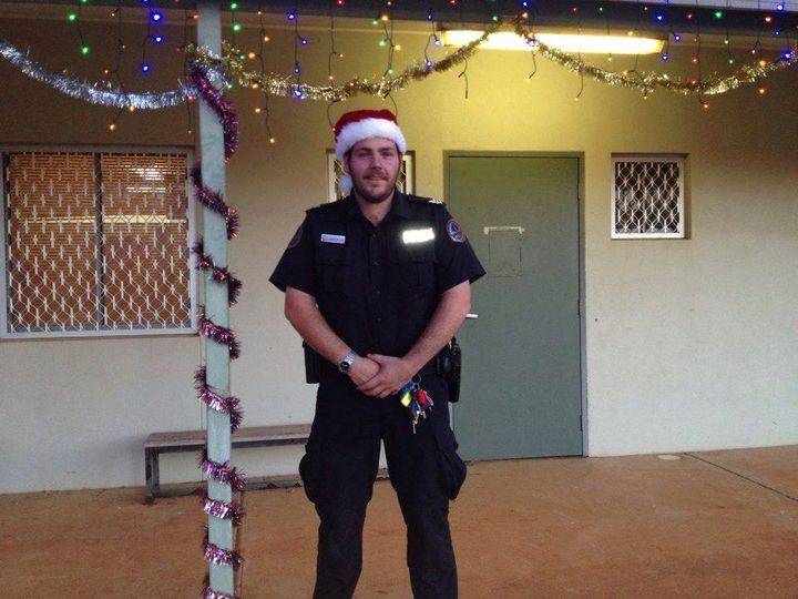 A police officer stands in front of a house in remote NT, decorated in Christmas items