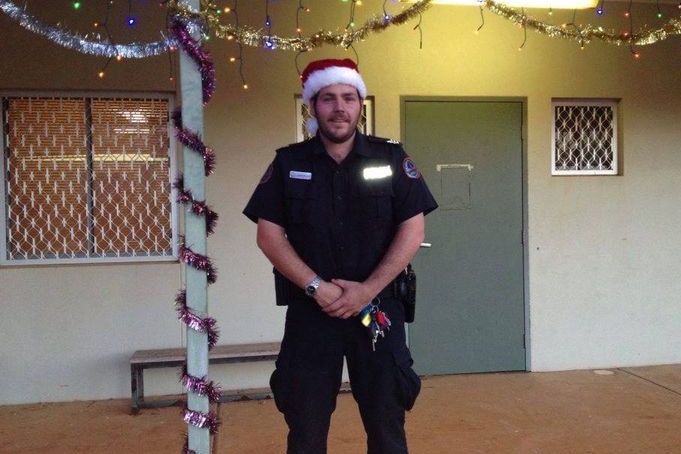 A police officer stands in front of a house in remote NT, decorated in Christmas items