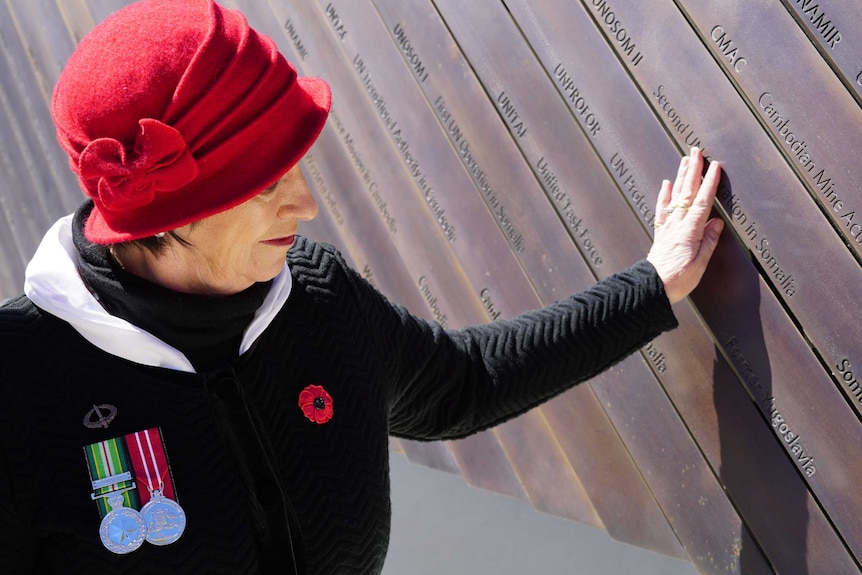 A woman touches a bronze panel on a memorial.