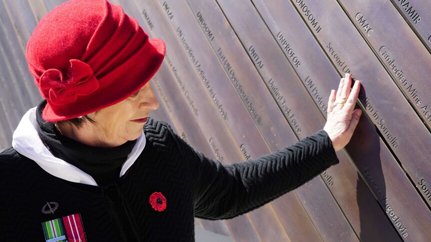 A woman touches a bronze panel on a memorial.