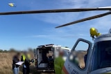 Helicopter flies over an ambulance in a paddock