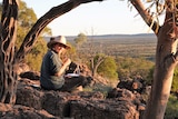 A lady with a hat on sitting on a rocky ledge overlooking the outback