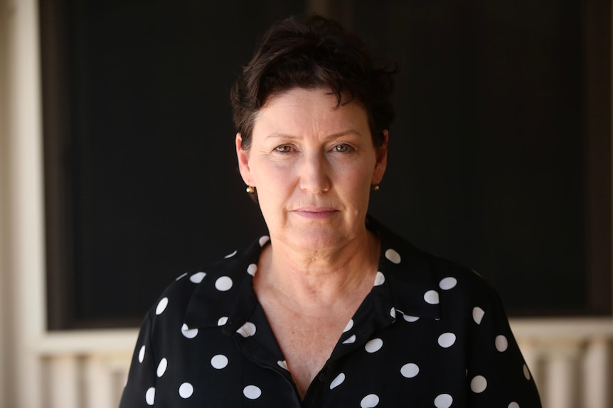 A woman with short brown hair and a black top with white dots look at the cnmera