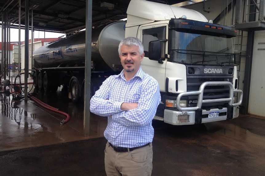 A man stands in front of some milk trucks with his arms folded.