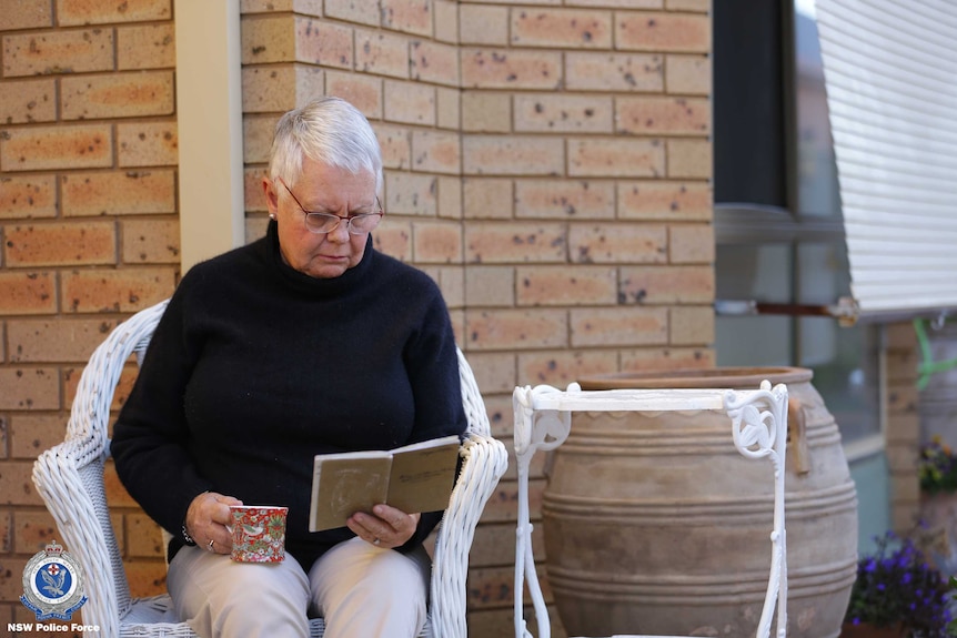 A lady reading a diary holding a cup of tea.