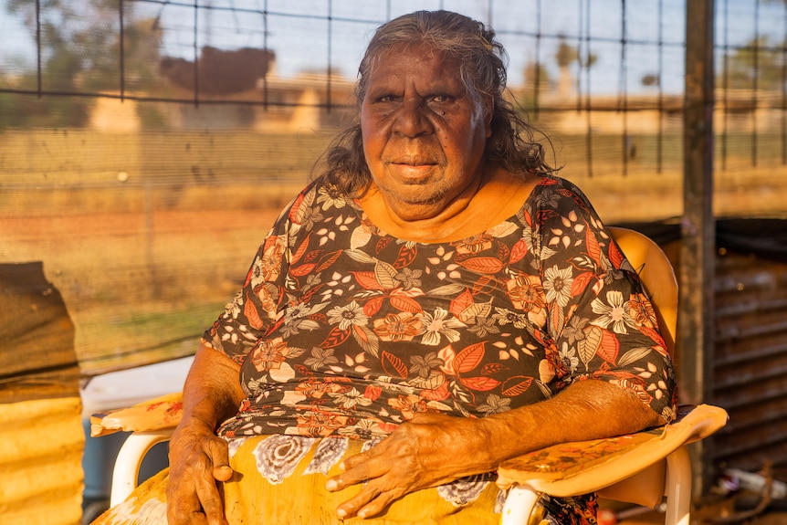 Elder Wendy Nungarrayi Brown looks at the camera while sitting on a chair.
