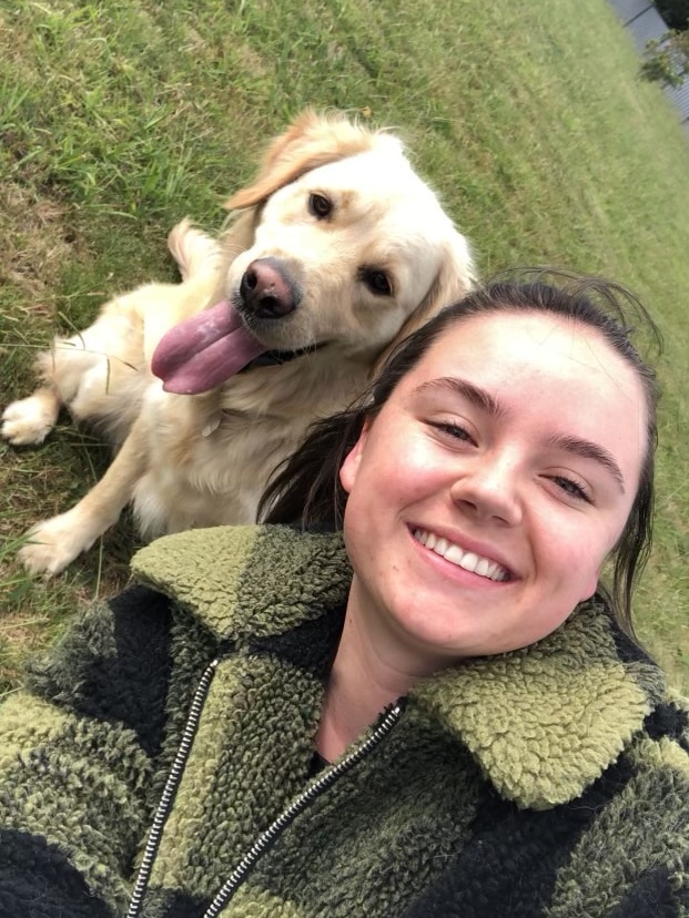 A selfie of a young woman in a shearling jacket with a golden retriever.