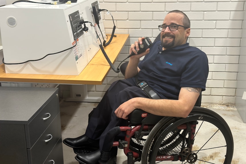 man sitting in a wheelchair smiling, sitting at a radio communications table