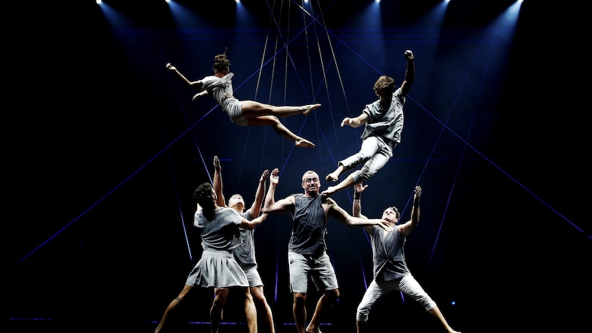 Acrobats perform on a darkened stage
