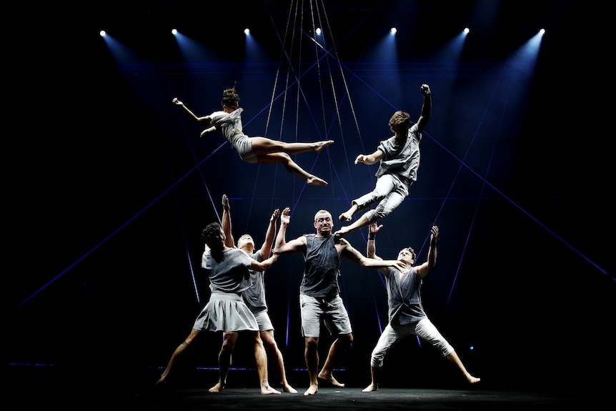 Acrobats perform on a darkened stage