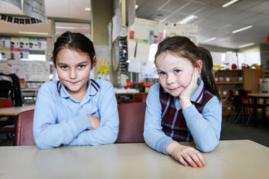 Year One students, Leila and Ruby sit at a classroom desk in school uniforms.