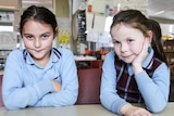 Year One students, Leila and Ruby sit at a classroom desk in school uniforms.
