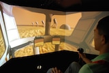 A man sits in a simulator, driving a vehicle on mars.