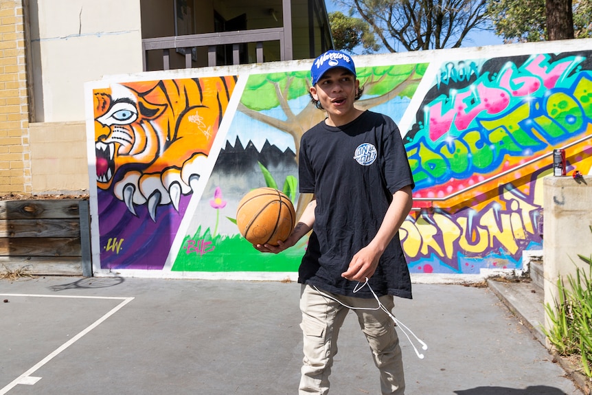 Eddie Fejo bounces a basketball as he moves across a court, in front of a brightly coloured mural with a tiger.