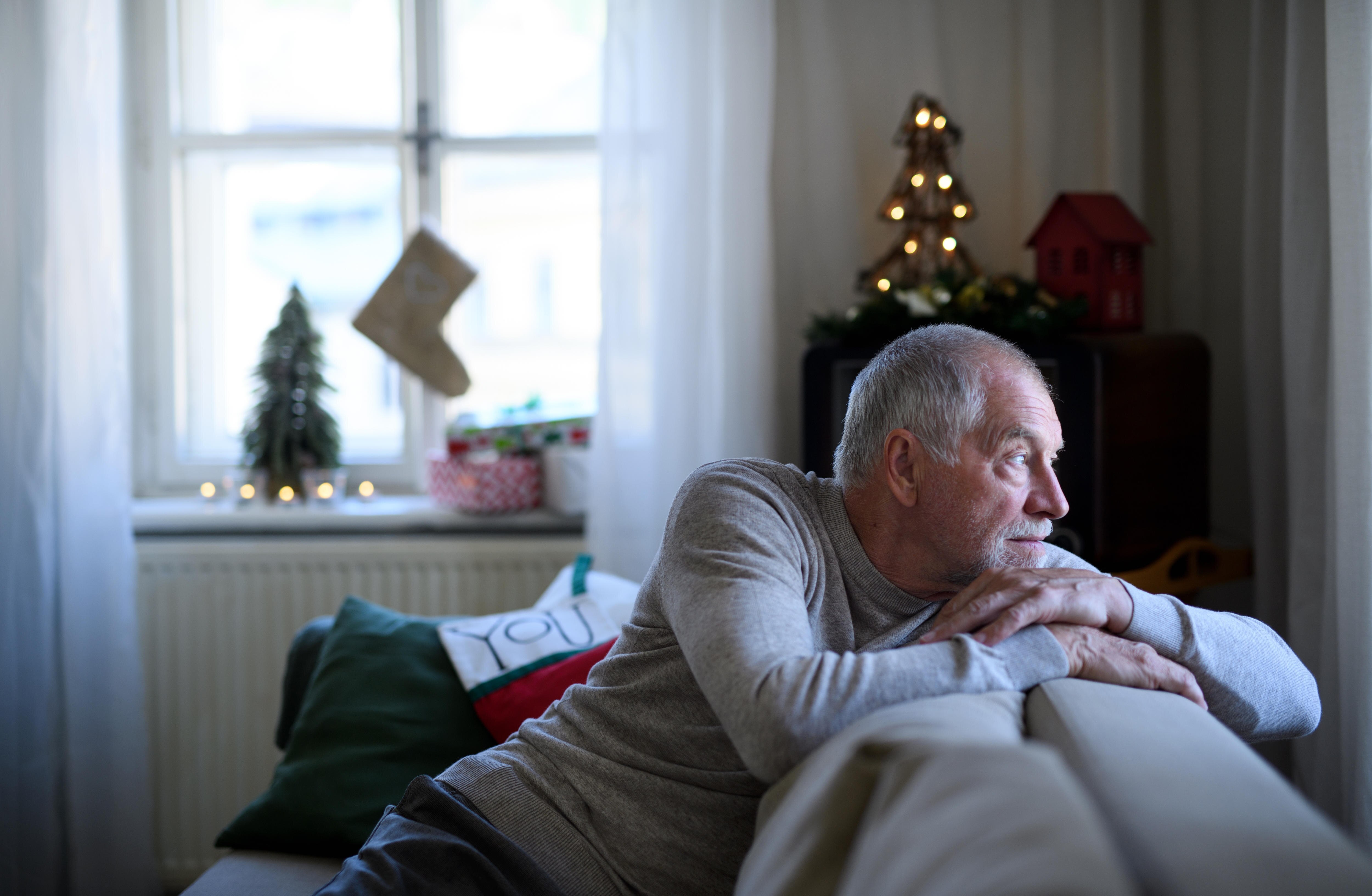 Lonely senior man sitting on sofa indoors at Christmas, solitude concept