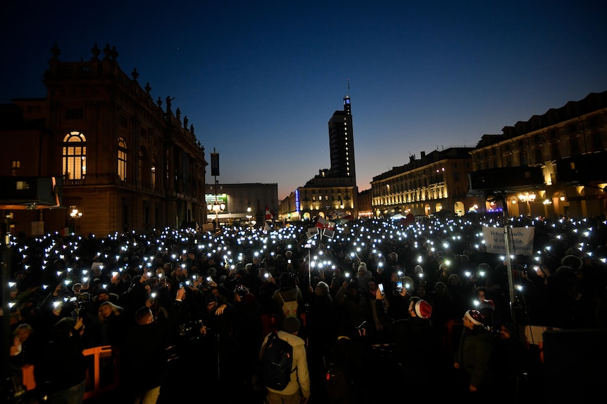 Large group of people in Italy gathering outside shining their phone torch lights 