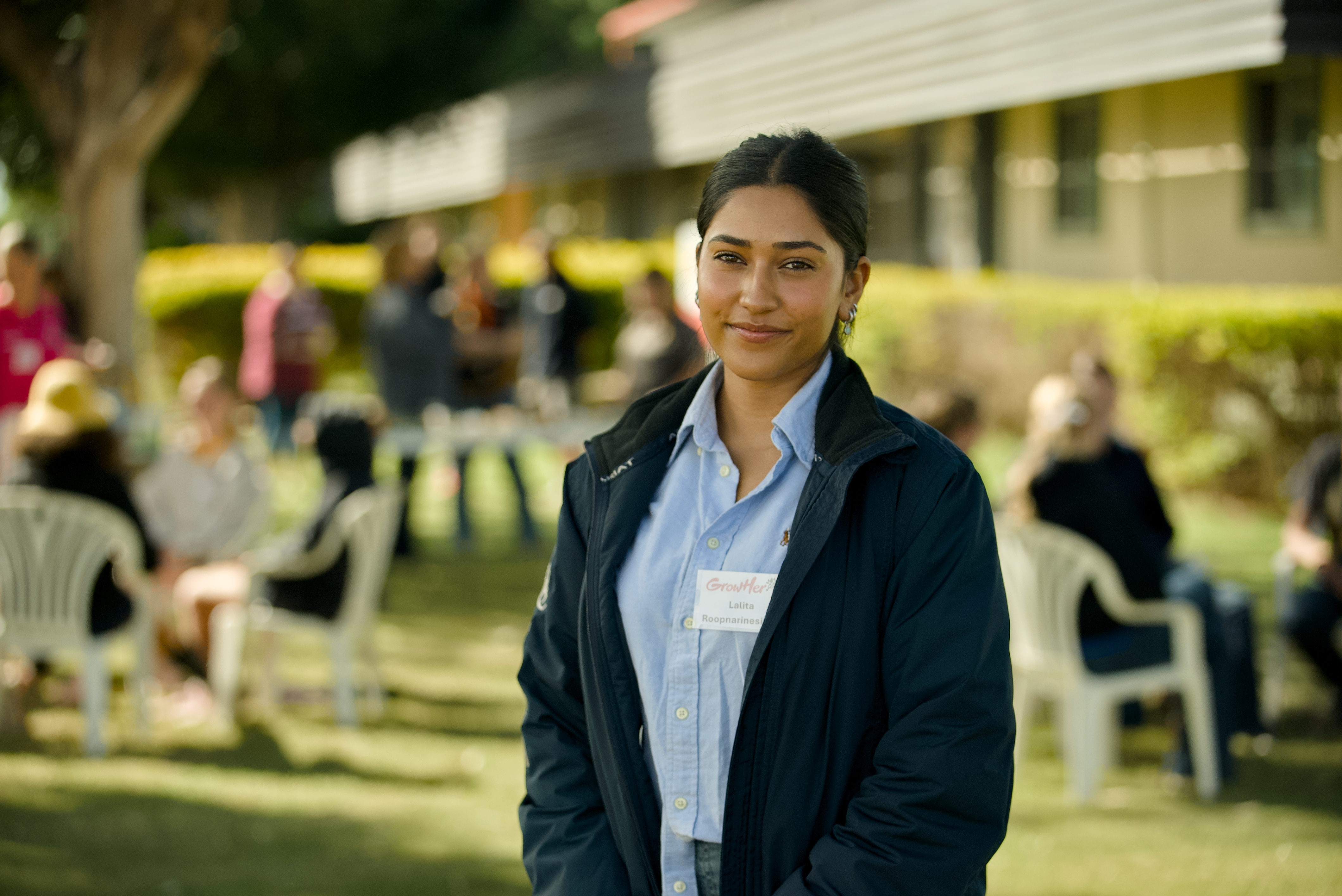 A younger woman stands in front of park with other students blurred in background.