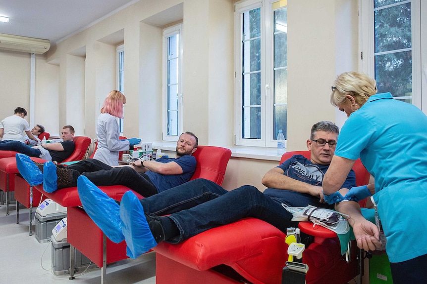 People donate blood in a row of chairs as nurses attend to them.