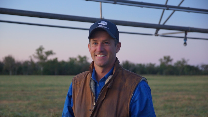 Image of a man smiling in front of green paddocks.