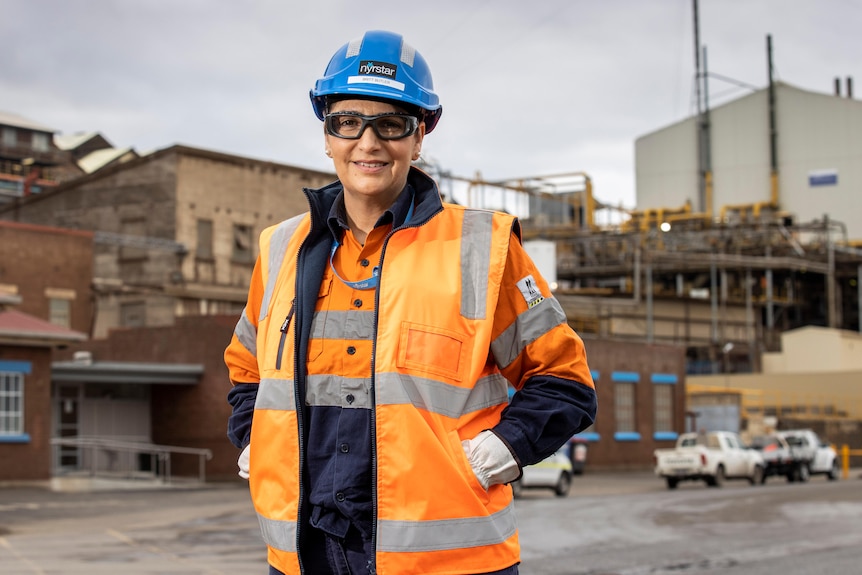 A woman in hard hat and high-vis gear stands outside a factory.